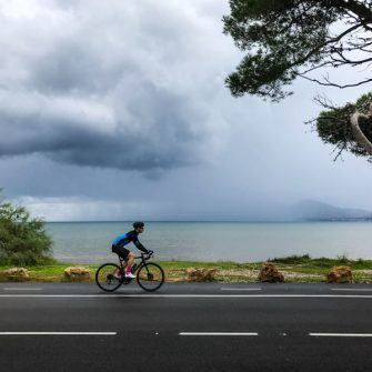 Cyclist cycling around Pollensa bay in rainstorm