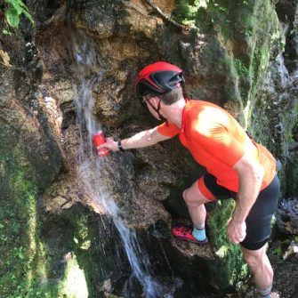 Cyclist filling water bottle from waterfall