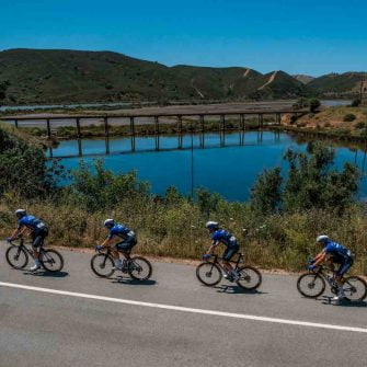Four cyclists riding a bicycle by side lake on Tour of Algarve