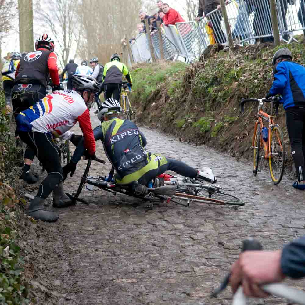 A cyclist falls on a brick road and is pulled by another cyclist cycling tours belgium